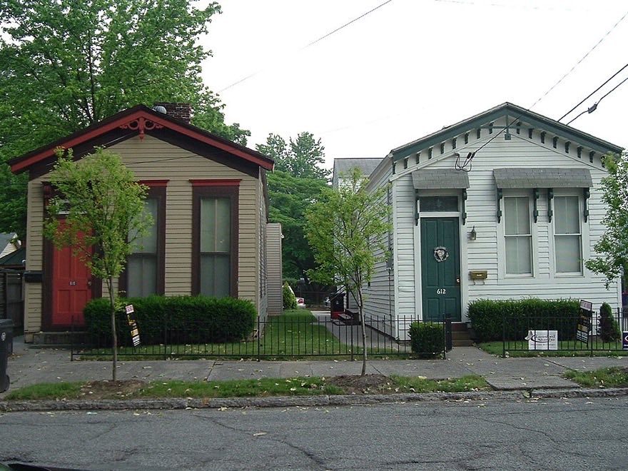 A pair of single-storey shotgun houses on a narrow lot in Old Louisville, one cream with red trim and one pale green, both with decorative eave brackets